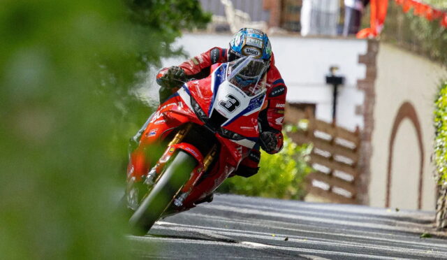 Motorcycle racer in red gear leaning through a sharp turn on a narrow street, helmeted rider on a red sportbike with number 3.