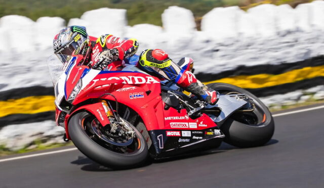 Motorcycle racer on a red Honda sportbike leaning into a turn on a race track