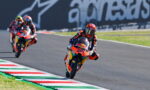 Rider on orange race bike #51 leans into a curve on a racetrack, with other racers following in the background.