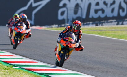 Rider on orange race bike #51 leans into a curve on a racetrack, with other racers following in the background.