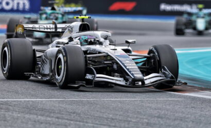 Silver Formula 1 car on a race track turning a corner, with another car visible in the background, branding on the car clear.
