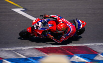 Motorcycle racer in red and blue livery leaning into a sharp turn on a race track.