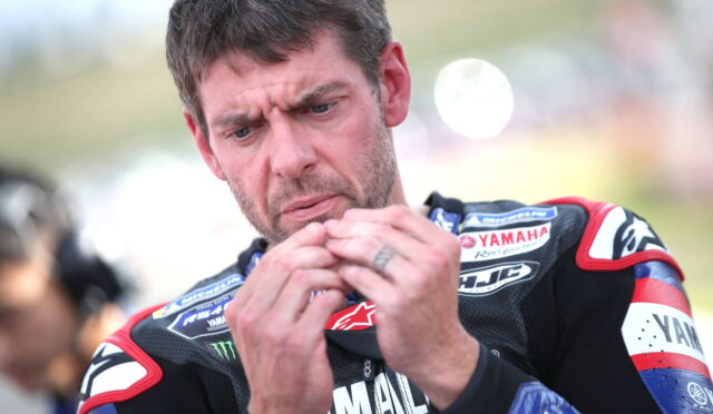 Motorcycle racer in Yamaha gear concentrates while handling a small object in his hands before a race.