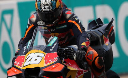 MotoGP rider leaning into a turn on a numbered race bike (26) with Red Bull livery and sponsor decals.