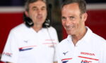 Smiling man in a white Honda polo shirt in the foreground with another team member wearing a headset in the background inside a red-paned pit area.
