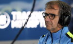 Radio host wearing glasses and headphones in a studio, speaking into a microphone.