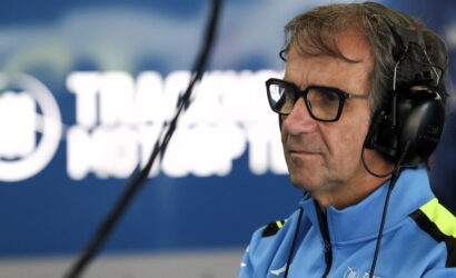 Radio host wearing glasses and headphones in a studio, speaking into a microphone.