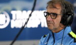 Side profile of a man wearing glasses and over-ear headphones in a recording studio, dressed in a blue jacket with neon accents.