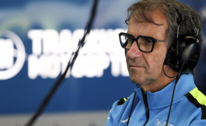 Side profile of a man wearing glasses and over-ear headphones in a recording studio, dressed in a blue jacket with neon accents.