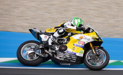 Racing motorcyclist in a white-black suit leans into a turn on a yellow sport bike on a blue-track background, helmet neon-green and white.](#) but without link