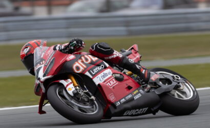 Red Ducati racing motorcycle leaning into a sharp corner on a track with rider in full suit and helmet close to the ground.",