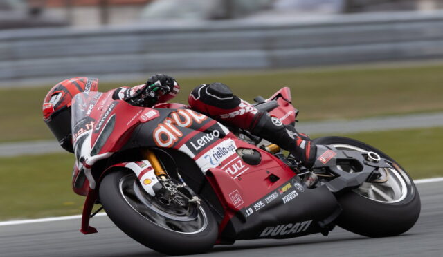 Red Ducati racing motorcycle leaning into a sharp corner on a track with rider in full suit and helmet close to the ground.",