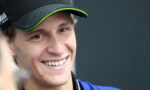 Close-up of a smiling man wearing a black cap with neon-green trim, looking slightly to the side.