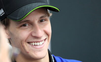 Close-up of a smiling man wearing a black cap with neon-green trim, looking slightly to the side.