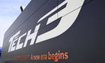 Close-up of a dark wall with a large white 'TECH' logo and the orange slogan 'A new era begins' beneath it.