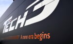 Close-up of a dark wall sign with a large white 'Tech' logo and the orange tagline 'A new era begins'.