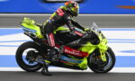 Rider in a black and neon-yellow racing suit on a lime-green race bike speeding along a racetrack, sponsor logos visible on the bike and suit.
