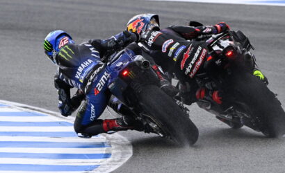 Two motorcycle racers lean into a sharp turn, one in blue Yamaha gear and the other in black-red, close behind on a race track.