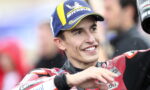 Person in a red racing suit and blue Michelin cap smiles while celebrating with arms raised.3c6️ Likely a motorsport winner or podium moment.