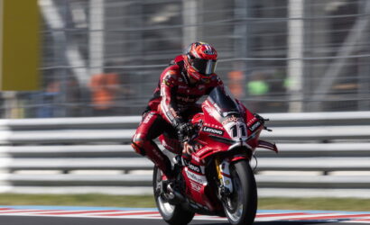 Moto race: rider in red suit on a red motorcycle with number 11 on a race track, leaning into a turn