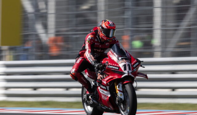 Moto race: rider in red suit on a red motorcycle with number 11 on a race track, leaning into a turn