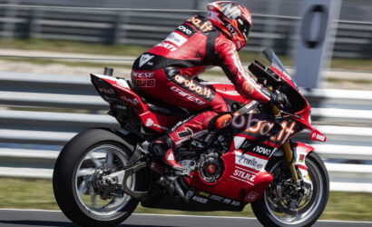Rider in red racing suit on a red Ducati race bike speeding along a racetrack.