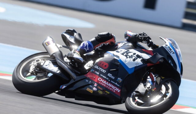 Motorcycle racer leaning into a turn on a racing track, full-suit and helmet with sponsor logos visible