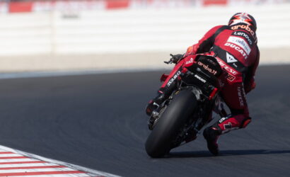 MotoGP rider in red Ducati leans into a high-speed corner on a race track, tires gripping the asphalt.
