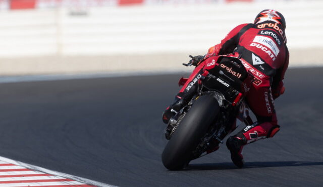 MotoGP rider in red Ducati leans into a high-speed corner on a race track, tires gripping the asphalt.