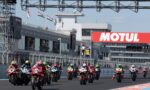 Motorcycle racers sprinting off the starting line on a straight track with a large Motul banner in the background