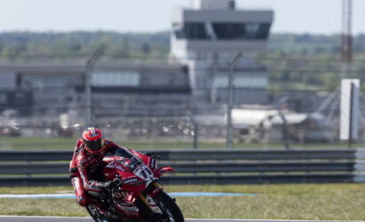 MotoGP rider in red leans into a turn on a race track, red sponsored motorcycle in action with barriers in the background