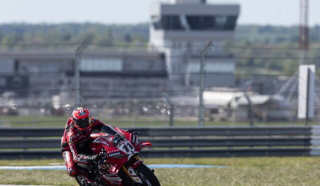 MotoGP rider in red leans into a turn on a race track, red sponsored motorcycle in action with barriers in the background