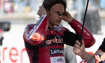 Moto racer in a red Aruba.it suit adjusts ear protection while a crew member holds an umbrella nearby.