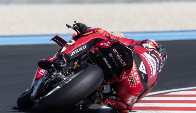 Motorcycle racer in red leathers leaning into a tight turn on a race track next to red and white curb marks.