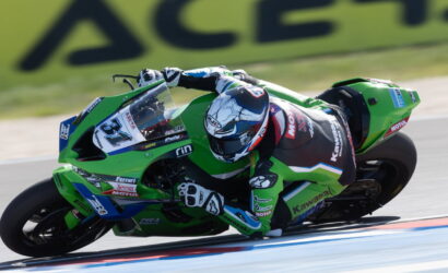 Rider on a green Kawasaki racing bike leaning into a sharp turn on a race track, full sprint position with helmet and suit.