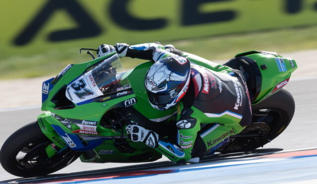 Rider on a green Kawasaki racing bike leaning into a sharp turn on a race track, full sprint position with helmet and suit.