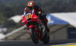 Motorcycle racer in red gear on a red bike with number 10 leaning into a turn on a race track