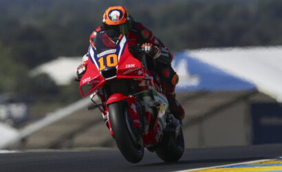 Motorcycle racer in red gear on a red bike with number 10 leaning into a turn on a race track