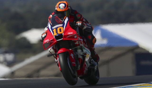 Motorcycle racer in red gear on a red bike with number 10 leaning into a turn on a race track