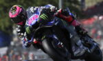 MotoGP rider in a pink-helmet race suit leans into a high-speed corner on a Yamaha motorcycle with Monster Energy and ENEOS branding