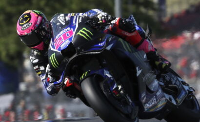 MotoGP rider in a pink-helmet race suit leans into a high-speed corner on a Yamaha motorcycle with Monster Energy and ENEOS branding