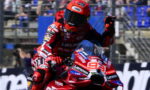 Rider in red Lenovo racing suit on a Ducati motorcycle, fist raised during high-speed action on the track.