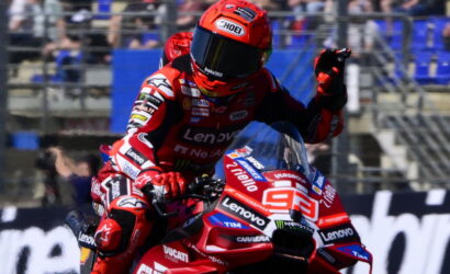 Rider in red Lenovo racing suit on a Ducati motorcycle, fist raised during high-speed action on the track.