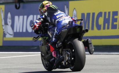 Motorcycle racer in blue Yamaha suit leaning into a corner on a racing track with Michelin banners in the background