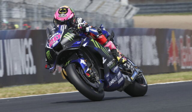 Professional motorcycle racer in a pink helmet leans into a turn on a Yamaha racing bike with Monster Energy livery.