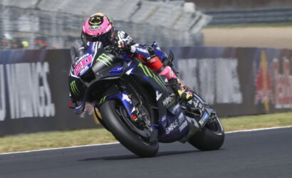MotoGP rider leaning into a left turn on a Yamaha race bike with pink helmet and Monster Energy livery.