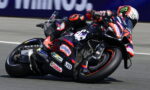 Motorcycle racer in gear leaning into a sharp turn on a sponsored sport bike during a race
