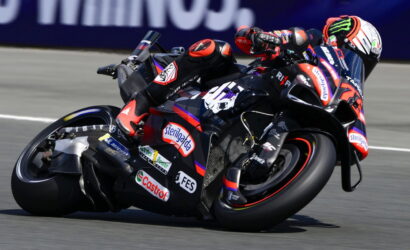 Motorcycle racer in gear leaning into a sharp turn on a sponsored sport bike during a race