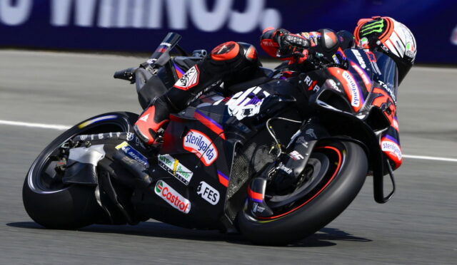 Motorcycle racer in gear leaning into a sharp turn on a sponsored sport bike during a race