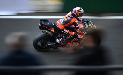 Motorcycle racer in orange Red Bull gear leaning into a turn on a racetrack